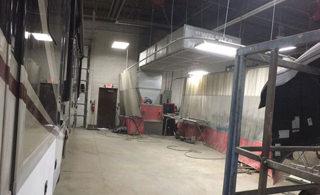The image shows an interior space with a large recreational vehicle  RV  parked inside a building, featuring a spacious living area with a couch and a television screen, a kitchenette with a countertop and sink, and a dining table with chairs.