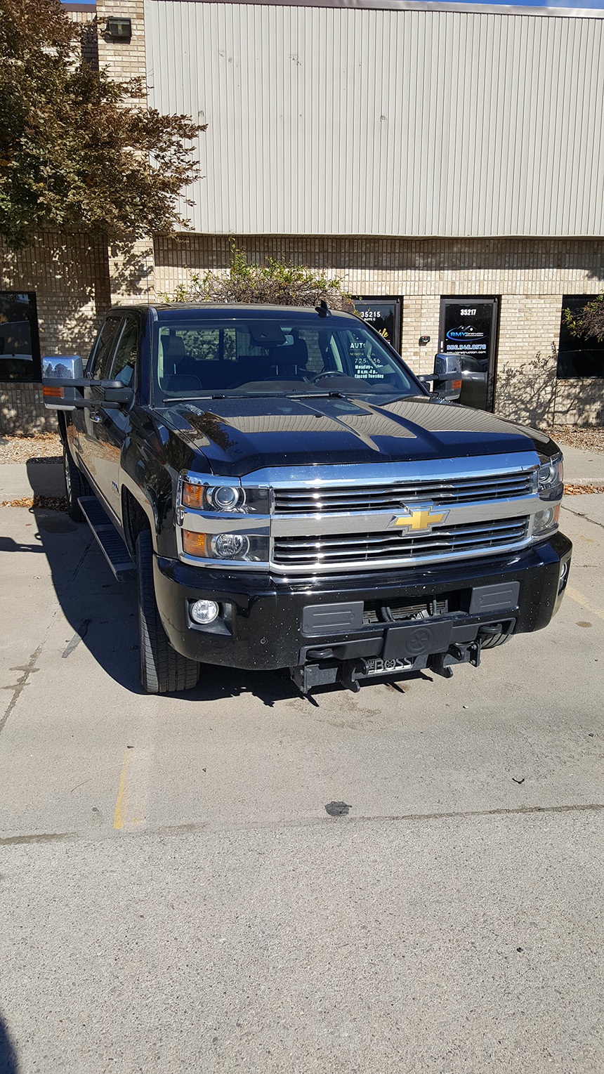 The image shows a black Chevrolet truck parked in a parking lot with a building in the background.