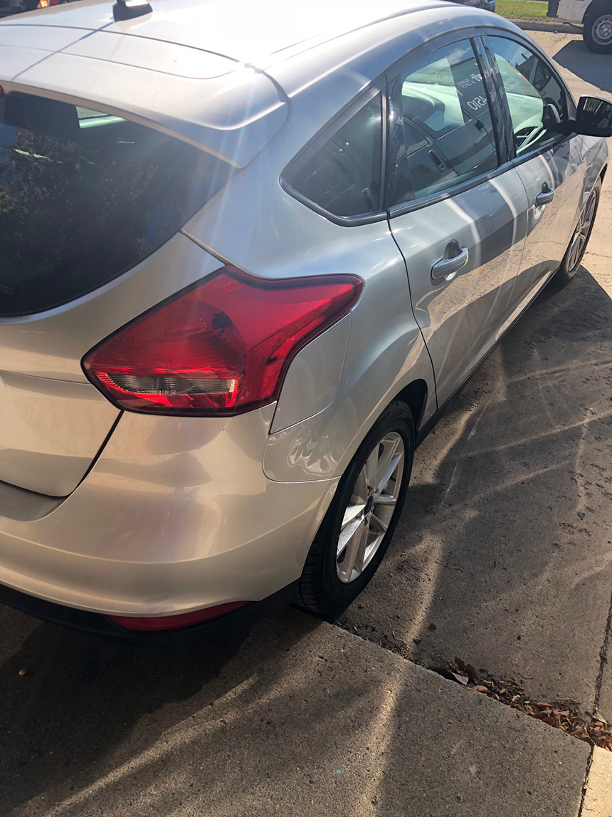 The image shows a silver-colored compact car parked outdoors during daylight.