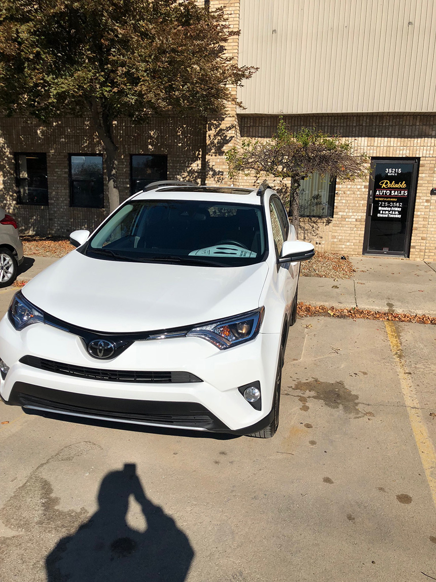 The image shows a white Toyota SUV parked in a parking lot with other cars visible in the background.